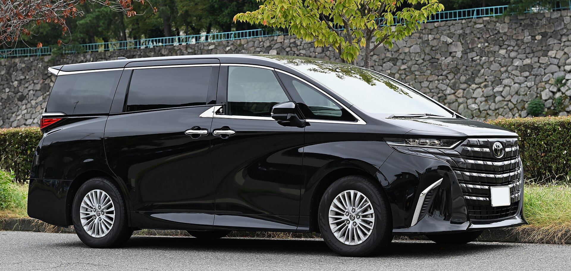 Black Toyota Alphard Hybrid (AH40) front three-quarter view against a stone wall
